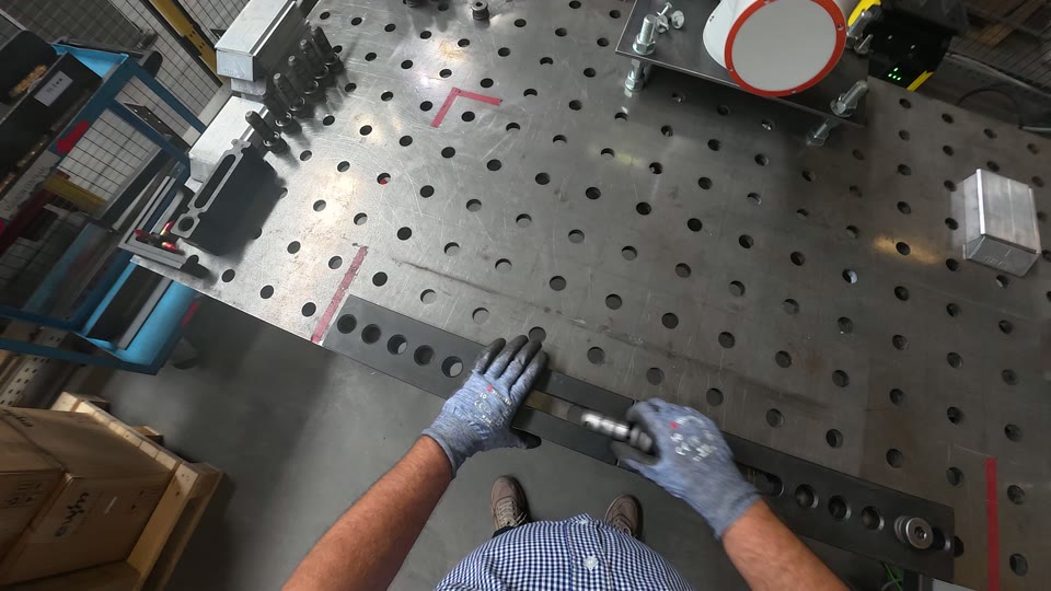 Handen leggen een staaf tegen de rode aanslag op de lastafel.