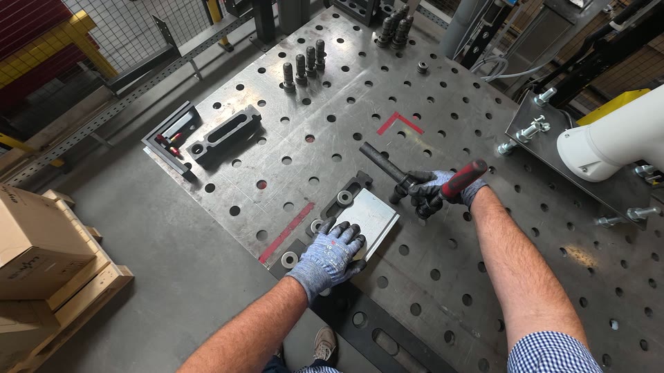 Handen spannen een werkstuk op met een klem op de lastafel.